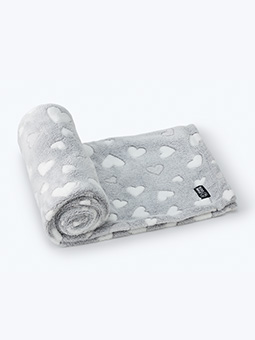 Szary, pluszowy koc dla psa w białe serca jest w części zwinięty w rulon, a w części rozłożony i leży na białym tle.