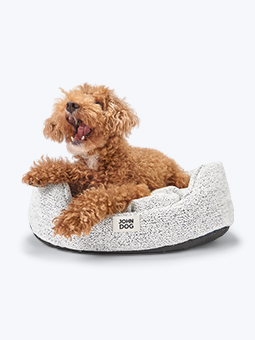 Legowisko owalne w kolorze jasno-szarym, dla psa. Widoczny leżący na nim pies rasy pudel toy. Marka John Dog.