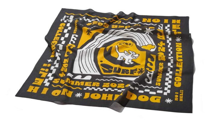 Apaszka dla psa marki John Dog z kolekcji NO I HEL, zawiązana w trójkątną formę. Na czarnym tle znajdują się żywe żółte i białe wzory, w tym pies na desce surfingowej, fale i napisy "Summer 2024 Collection".