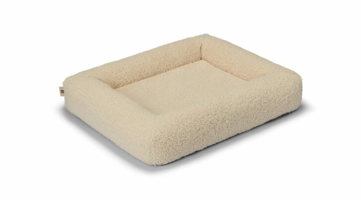 Czarno-biały pudel wygodnie leży na legowisku BALI WOOLY marki John Dog. Wysokie brzegi legowiska zapewniają mu poczucie bezpieczeństwa, a miękka i przytulna faktura materiału zachęca do relaksu.