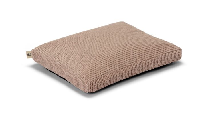 Mały jamnik o brązowej sierści leży na różowym, prostokątnym legowisku modelu WAVY marki John Dog, które zapewnia mu wygodę i wsparcie podczas odpoczynku.