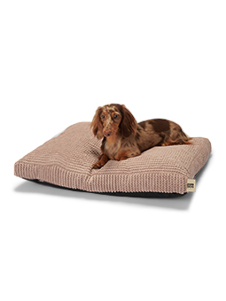 Mały jamnik o brązowej sierści leży wygodnie na różowym legowisku modelu WAVY marki John Dog. Legowisko ma fakturę w paski i miękki materiał, zapewniając psu komfort.