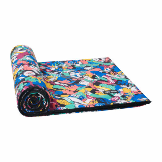 Zwinięty w rulon koc dla psa w intensywnie kolorowy wzór przedstawiający różnorodne postacie i rośliny. Krawędzie koca są czarne, a miękka czarna warstwa wewnętrzna wystaje delikatnie z rolki. Koc leży na białym tle, częściowo rozwinięty.