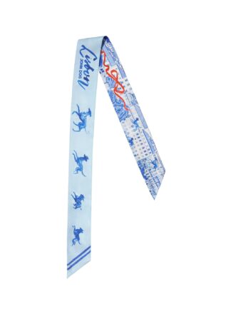 Cienka, dwustronna apaszka John Dog z kolekcji Lizbona w kolorze błękitnym ułożona na kształt odwróconej litery V. Z jednej strony są na niej rysunki granatowych psów rasy chart, a z drugiej rysunki granatowych kamienic z czerwoną wstążką.