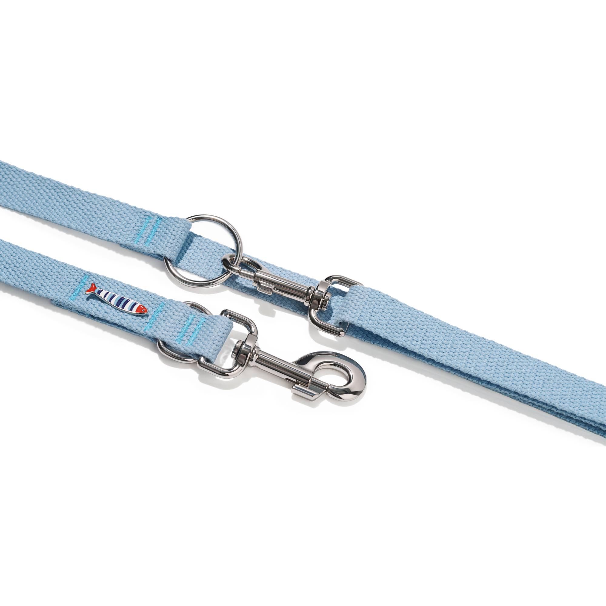 Zbliżenie na zapięcie smyczy przepinanej John Dog z kolekcji Lizbona w błękitnym kolorze. Pod nim znajduje się taśma w kolorze błękitnym z pinem w kształcie rybki i karabińczykiem.