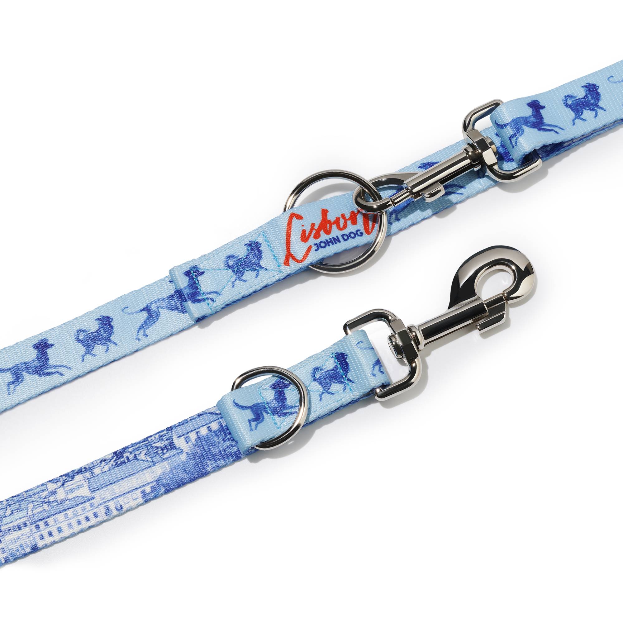 Zbliżenie na zapięcie smyczy przepinanej John Dog z kolekcji Lizbona we wzór z granatowymi psami na błękitnym tle z czerwonym napisem Lisbon. Pod nim znajduje się taśma we wzór z granatową panorama i karabińczykiem.