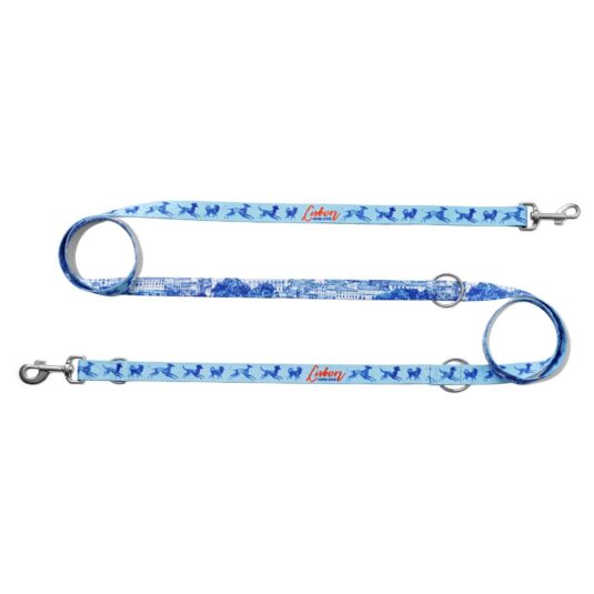 Smycz przepinana John Dog z kolekcji Lizbona we wzór z granatowymi psami i czerwonym napisem Lisbon po jednej stronie i rysunkiem panoramy miasta po drugiej stronie. Smycz rozłożona na płasko na kształt litery S, zawinięta po lewej i po prawej stronie w ślimak.