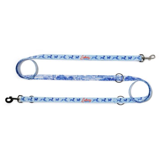 Smycz przepinana John Dog z kolekcji Lizbona we wzór z granatowymi psami i czerwonym napisem Lisbon po jednej stronie i rysunkiem panoramy miasta po drugiej stronie. Smycz rozłożona na płasko na kształt litery S, zawinięta po lewej i po prawej stronie w ślimak.