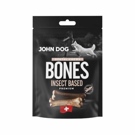 Czarne opakowanie przysmaków dla psów John Dog Bones Dental Chews Premium. Na opakowaniu znajduje się zdjęcie psa obok człowieka, grafika przysmaków w kształcie kości oraz symbol szwajcarskiej flagi.
